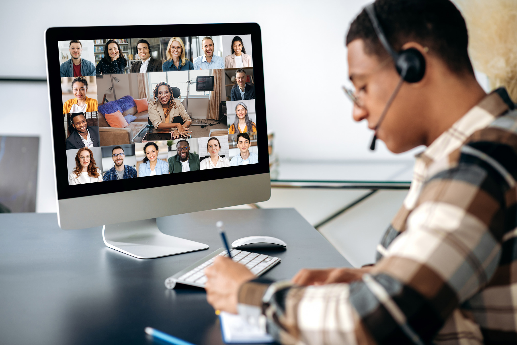 Successful male student learning distantly. At laptop screen female teacher and students. Teacher conducts online lecture, male student with headset takes notes. 